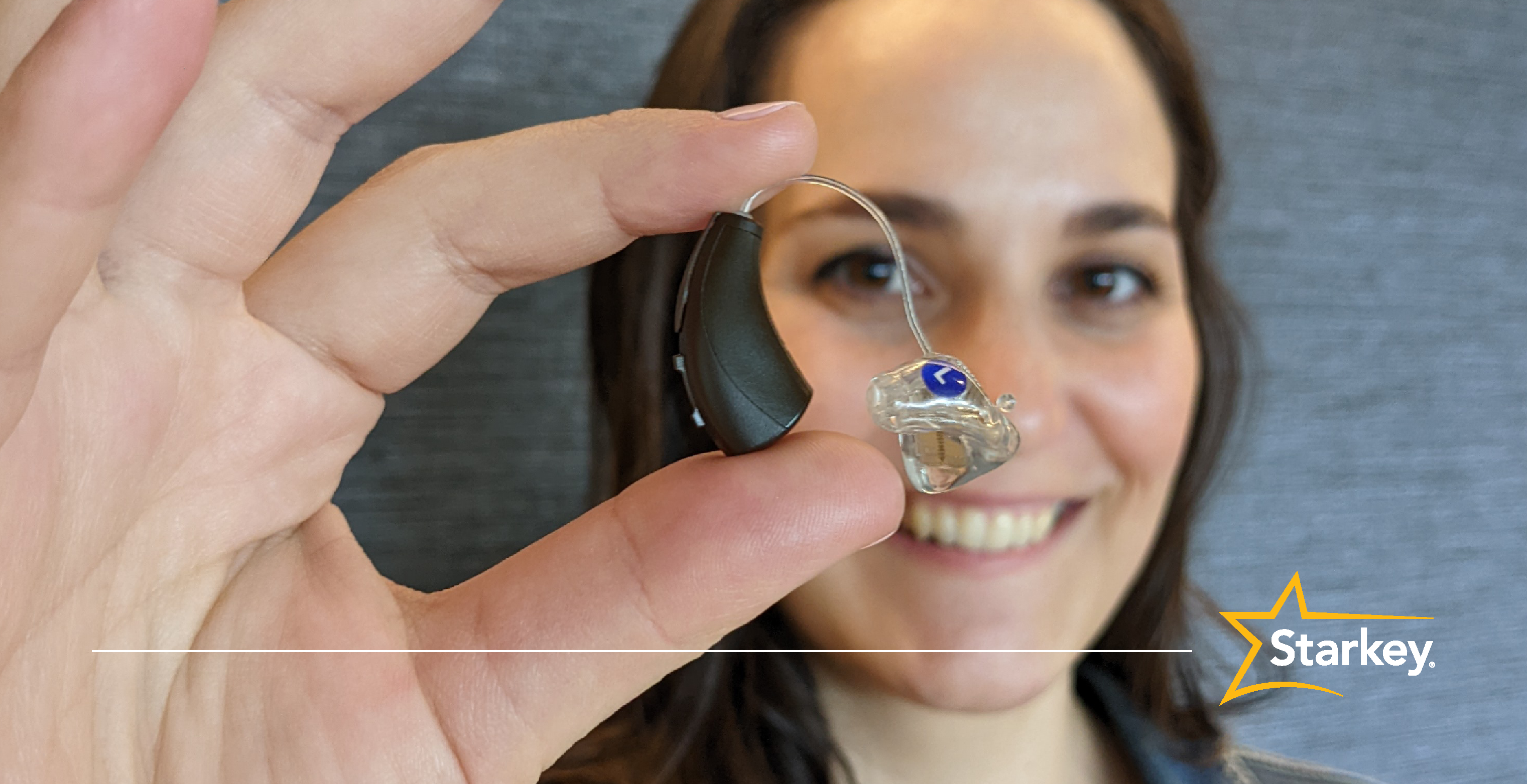 April Corner holds an espresso receiver-in-canal hearing aid in front of her right eye